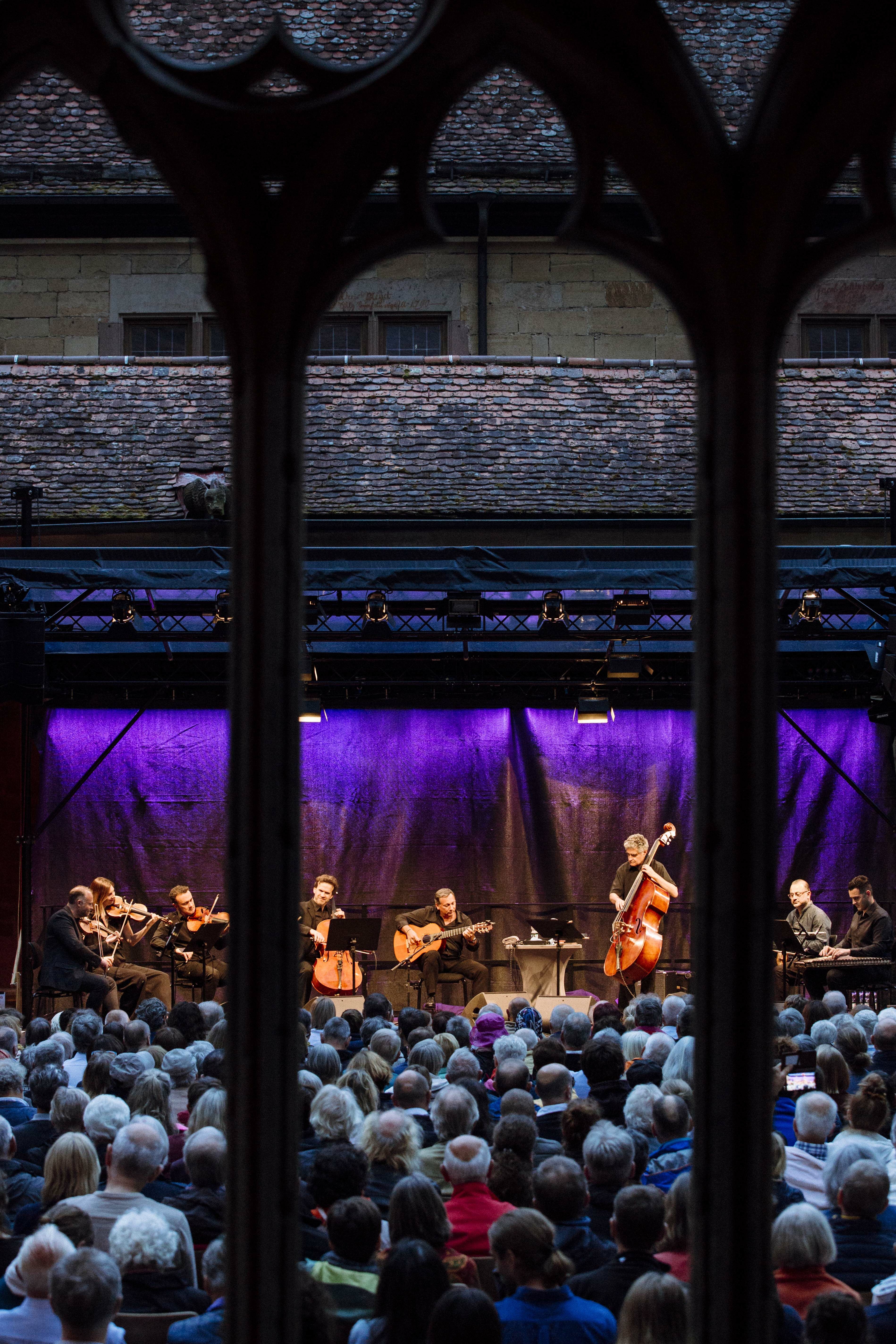 Blick durch Fenstersäulen einer Kirche auf eine Menschenmenge vor einer Bühne mit Musikern