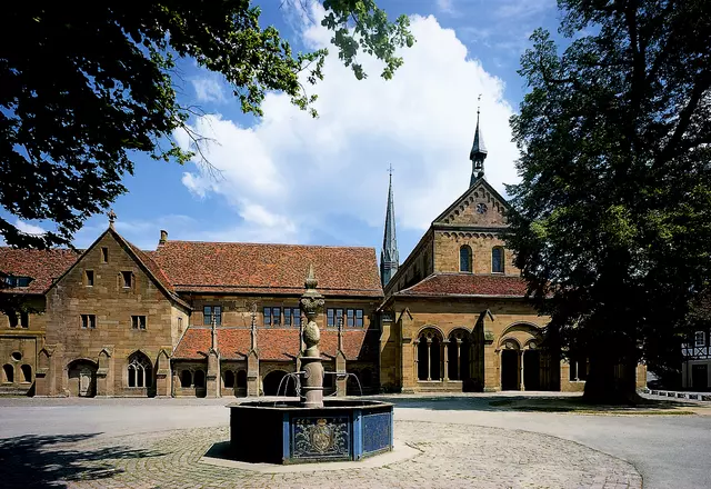 Blick auf die Klosterkirche mit Klausur, davor Brunnen und Lindenbäume